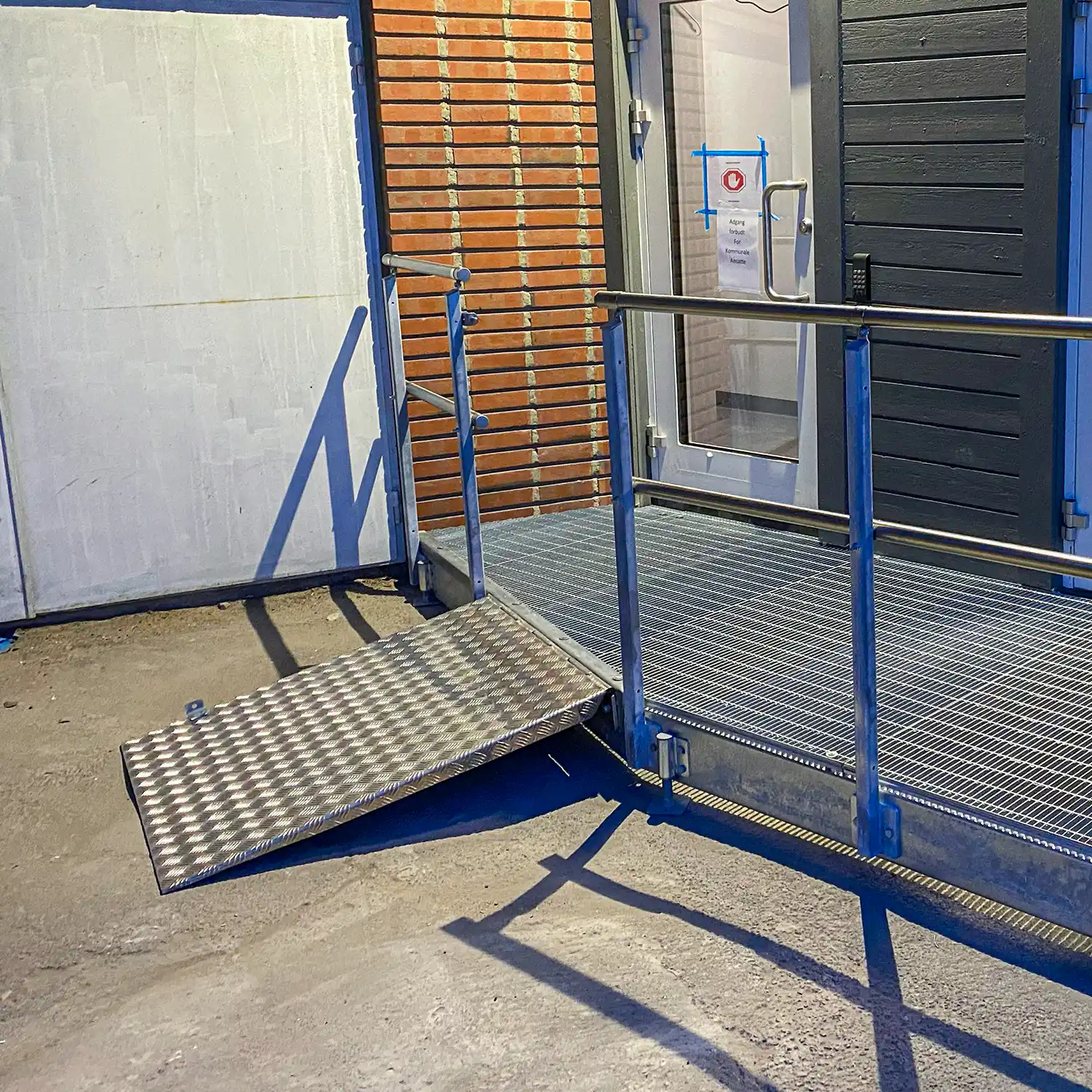 Bilde av en hengslet handicap-rampe, i posisjon nede og klart til bruk.