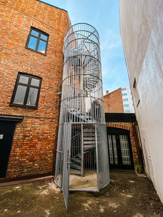Utendørs spiraltrapp med heldekkende bur og dør for adkomstsikring. 