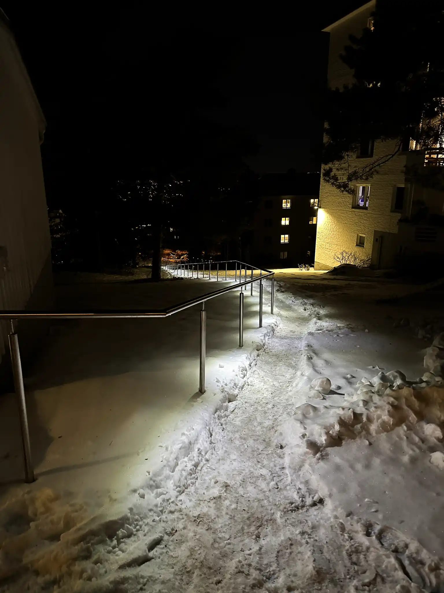 Håndløper på stender med LED-belysning i vintermørket på en snødekt sti..