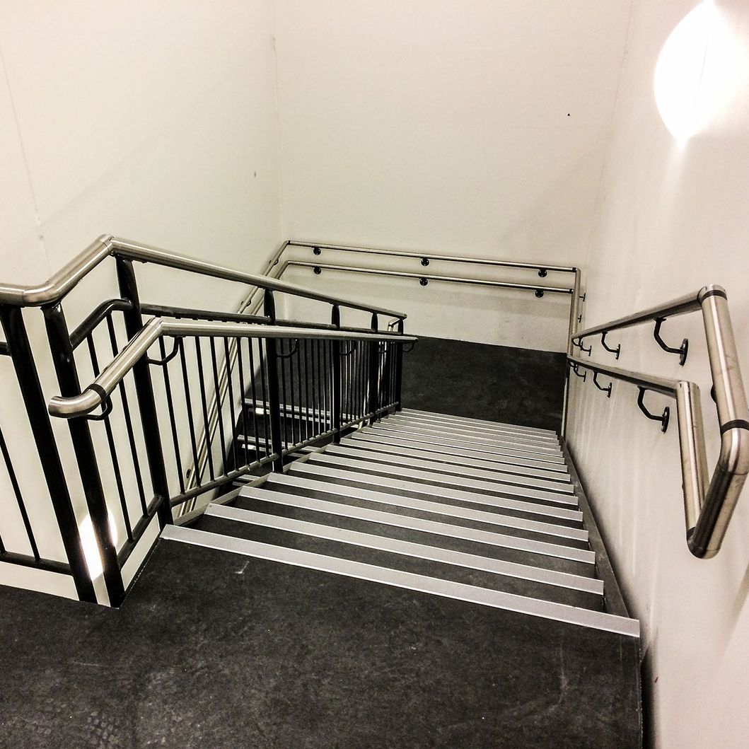 Svartlakkert trapp med doble rustfrie håndløpere og vertikale sprosser..