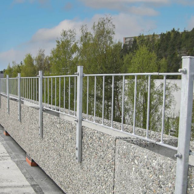 Lavt metallrekkverk som forhøyning på mur. Vertikale spiler..